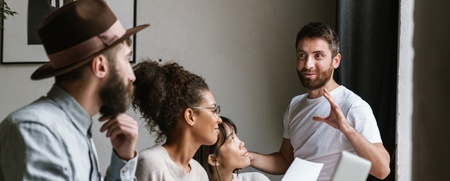 Fyra personer har ett möte vid ett bord, en man står och pratar medan de andra lyssnar.