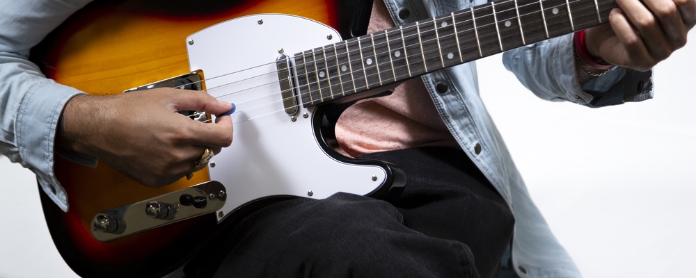 En person spelar elgitarr med en plektrum, närbild på händer och gitarr.