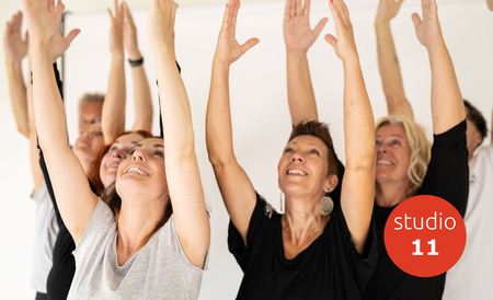 En grupp glada människor sträcker upp armarna i luften i en ljus studio. Röd cirkel med texten 'studio 11'.
