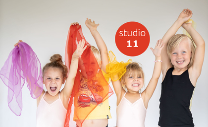 Fyra glada barn håller färgglada tygsjalar i luften framför en vit bakgrund med texten 'studio 11'.