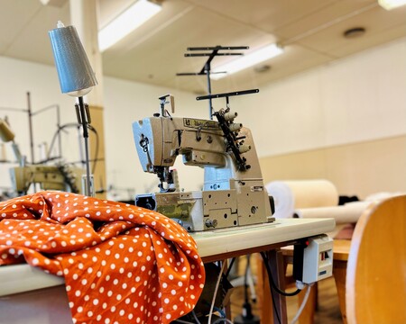 En industrisymaskin med orangeprickigt tyg på ett bord i en ljus syateljé.