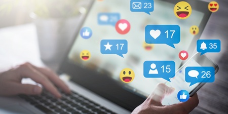 En person använder både en laptop och en smartphone med sociala medie-ikoner och notiser på skärmen.