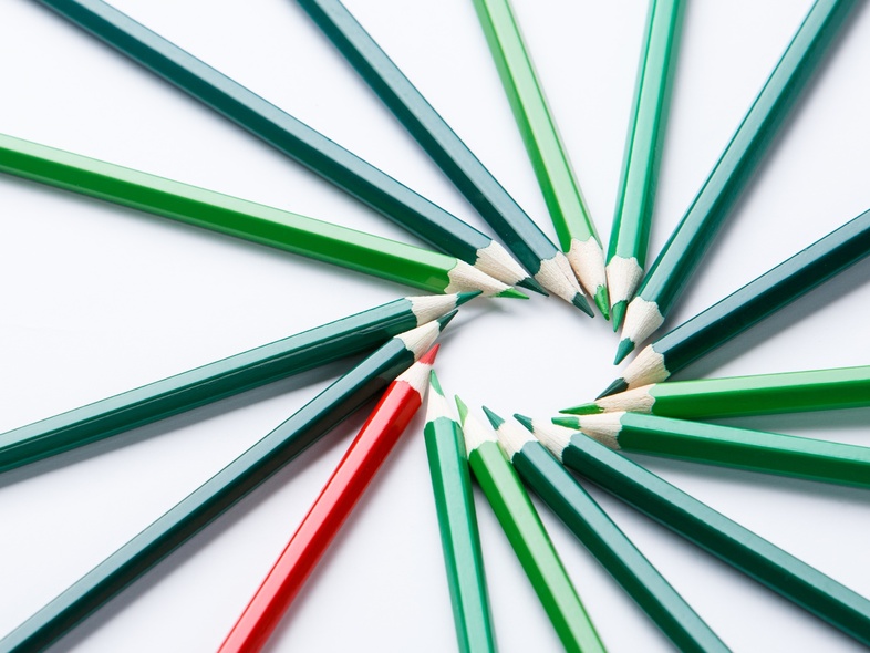 Flera gröna och en röd färgpenna ligger i en cirkel på ett vitt underlag.