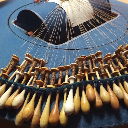 Närbild av en spetsknypplingsdyna med många trådar och träspolar, används för att skapa spetsmönster.