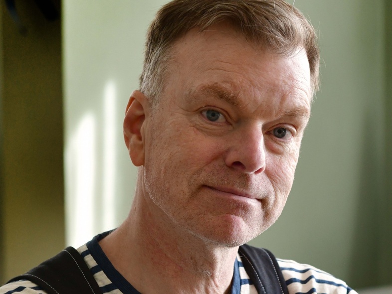 Porträtt av person med kort hår, blårandig tröja och hängslen