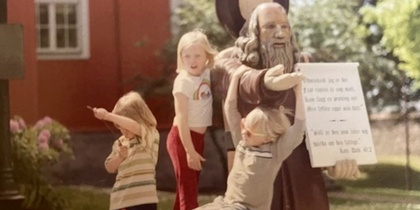 Tre barn poserar vid en staty utomhus.