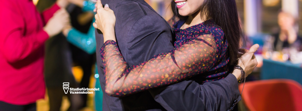 Två personer dansar nära varandra på en social tillställning, leende och festlig stämning.