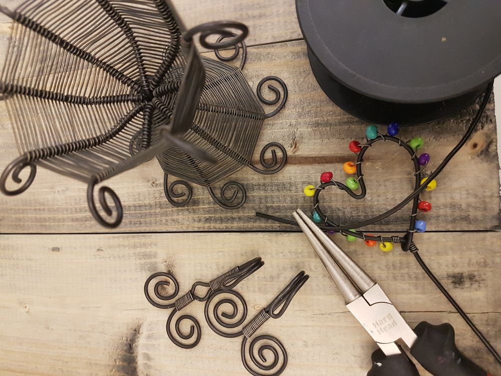 Verktyg och material för smyckestillverkning med ståltråd och färgglada pärlor på ett träbord.