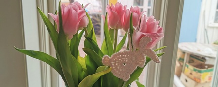 En bukett rosa tulpaner i vas står på ett fönsterbräde, dekorerad med en virkad kanin.