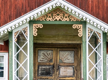 Entré till ett rött trähus med snickarglädje, gröna detaljer och dubbeldörrar i trä.