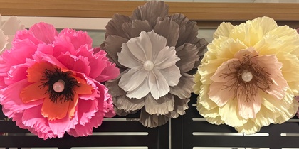 Fem stora, färgglada pappersblommor sitter fast på en svart skärm framför en spegel.