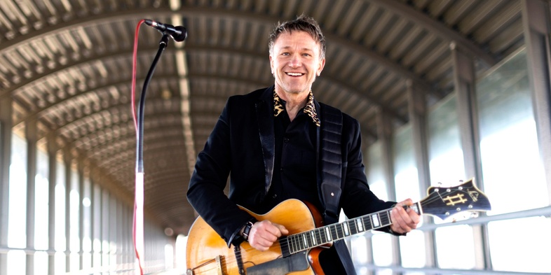 Mårten spelar gitarr och sjunger vid en mikrofon på en täckt gångbro med metalltak.