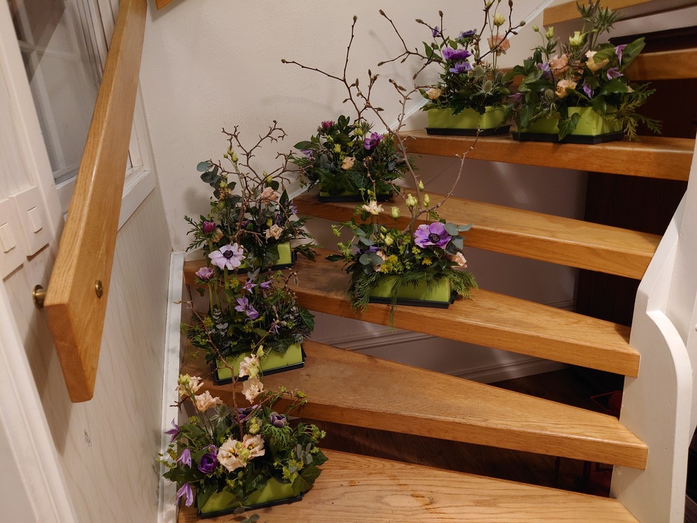 Trätrappa med flera blomarrangemang i gröna lådor placerade på stegen.