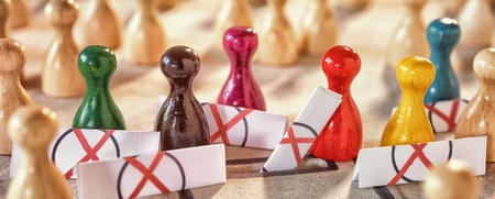 Färgade spelpjäser står i en grupp omgivna av barriärer med röda kryss, fler pjäser i bakgrunden.