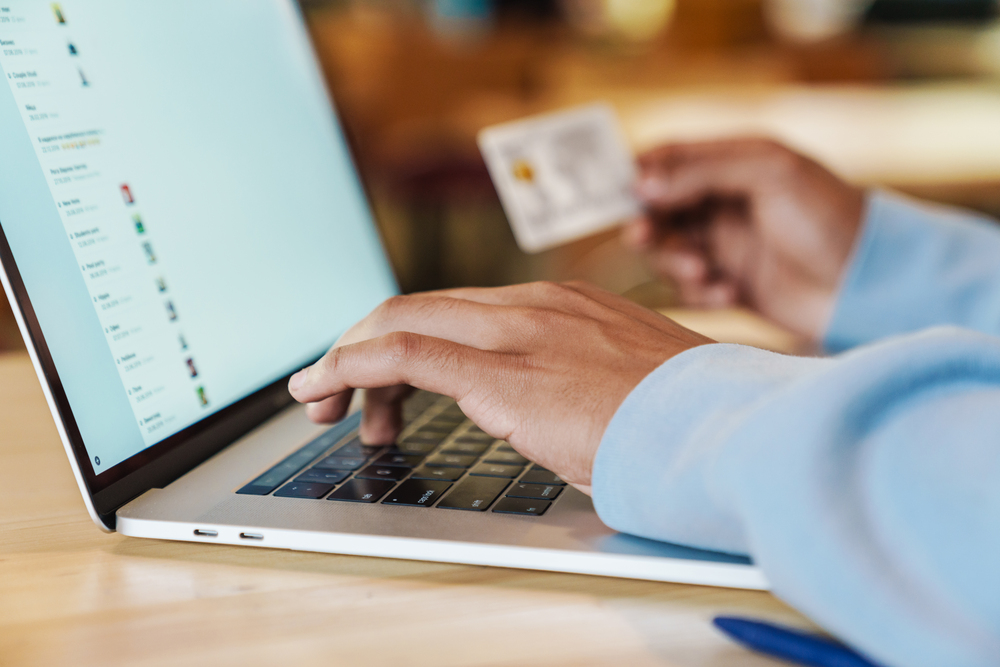 En person använder en bärbar dator och håller ett kreditkort, troligen för onlineköp.