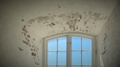 Ett gammalt fönster med välvt tak och avflagad puts på väggarna, ljusblå himmel utanför.