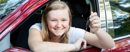Ung kvinna sitter i en röd bil och håller upp en bilnyckel med ett leende.