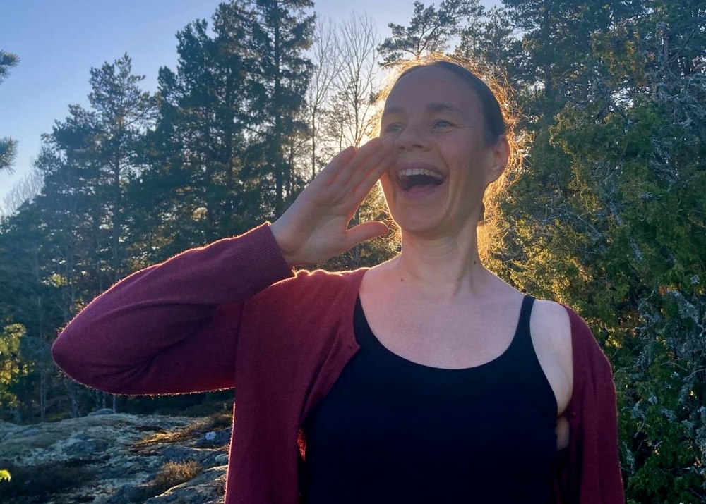 Person utomhus i skogsmiljö, håller ena handen vid ansiktet, ansiktet är suddat.