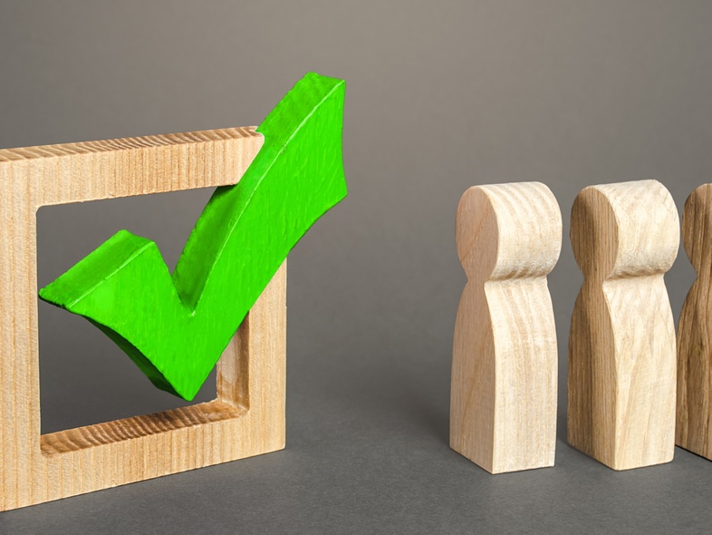 Träfigurer står bredvid en stor grön bock i en träram mot grå bakgrund.