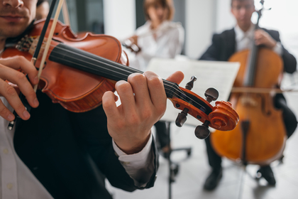 Närbild på en violinist som spelar i en liten orkester, med andra musiker i bakgrunden.