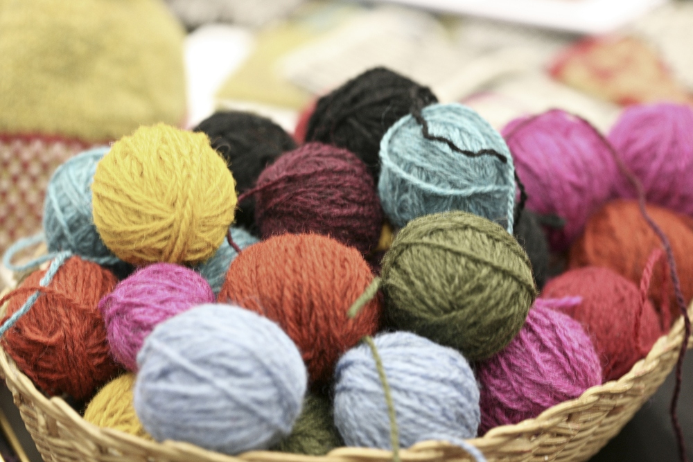 En korg fylld med garnnystan i olika färger, bland annat gult, blått, grönt och rött.