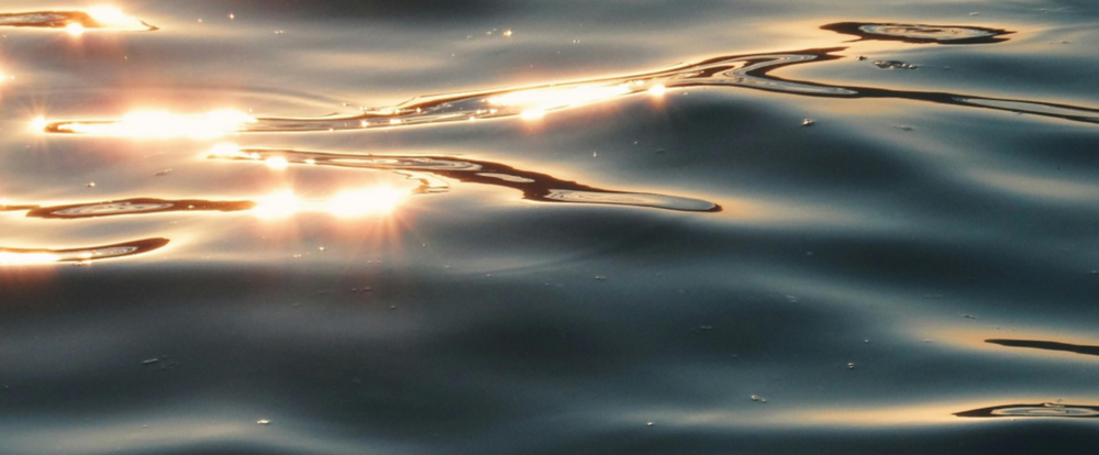Solreflektioner glittrar på mjuka vattenvågor i närbild.
