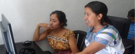 Två kvinnor i traditionella kläder sitter vid en dator och arbetar tillsammans i ett ljust rum.