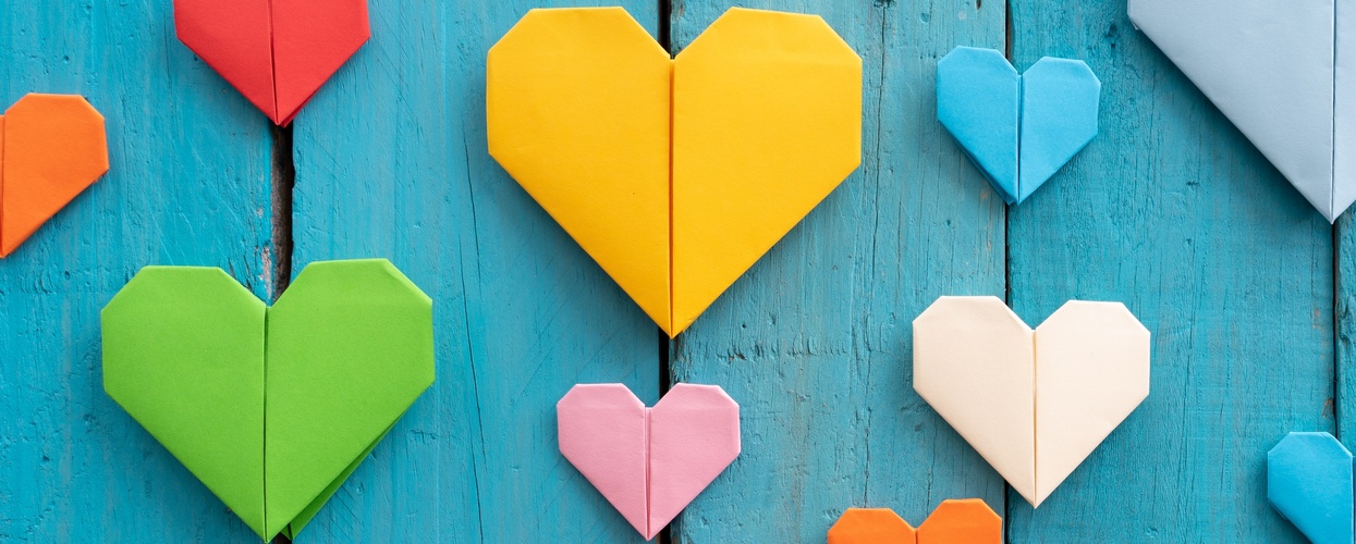 Flera färgglada origamihjärtan i olika storlekar på en blå träbakgrund.