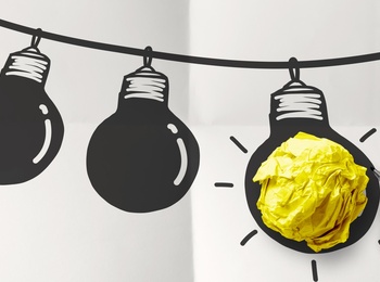 En hand ritar en glödlampa på ett papper, där en gul pappersboll används som glödlampans ljus.