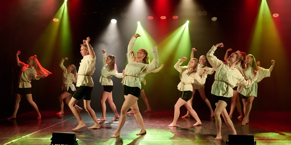 En grupp dansare uppträder på scen med färgglada strålkastare och synkroniserade rörelser.