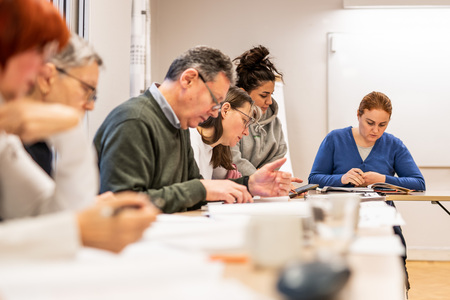 En grupp vuxna sitter vid ett bord och studerar tillsammans i ett klassrum.