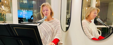 Kvinna spelar keyboard och sjunger i mikrofon, speglas i en rund spegel på väggen.