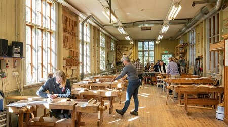 Ljust snickeriverkstad med flera personer som arbetar vid träbänkar.