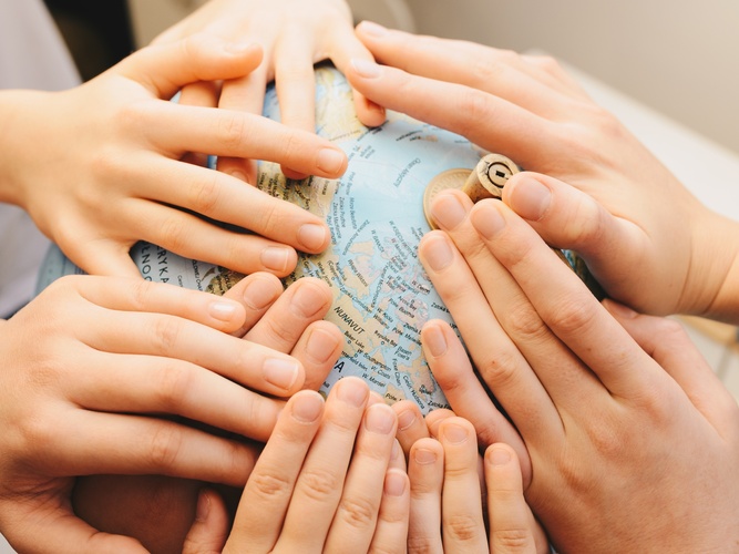 Flera händer från olika personer läggs ovanpå en jordglob.