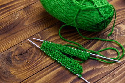 Grönt garnnystan och stickning på träbord med två stickor och påbörjat arbete.