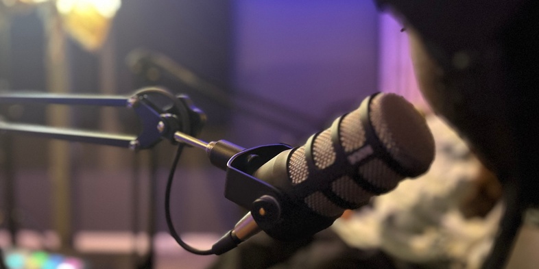 Närbild på en mikrofon i en studio med ljudutrustning och en person i bakgrunden.