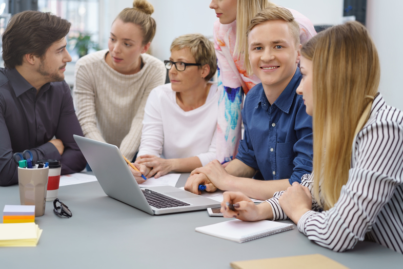 En grupp unga vuxna sitter runt ett bord och diskuterar vid en bärbar dator på ett kontor.