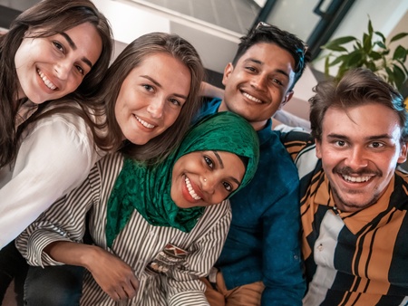 Fem unga vuxna sitter nära varandra i en soffa och ler mot kameran.