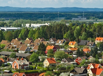 Färgglada villor med röda och gula tak i ett lummigt bostadsområde, omgivna av skog och berg i bakgrunden.