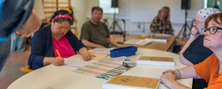 Personer sitter runt ett bord i ett klassrum och arbetar med papper och böcker.