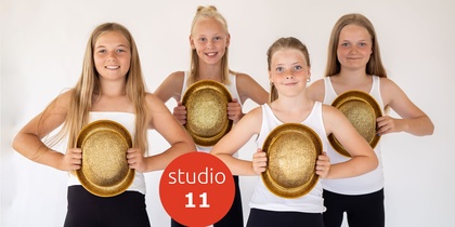 Fyra unga tjejer i vita linnen och svarta byxor håller gyllene hattar framför sig, står mot vit bakgrund.