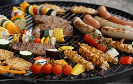 En grill fylld med olika sorters kött, korv, grönsaksspett och majskolvar utomhus.