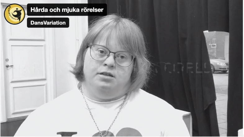 Person med axellångt hår sitter inomhus framför en dörr och ett svart draperi. Text om dansvariation syns i bilden.