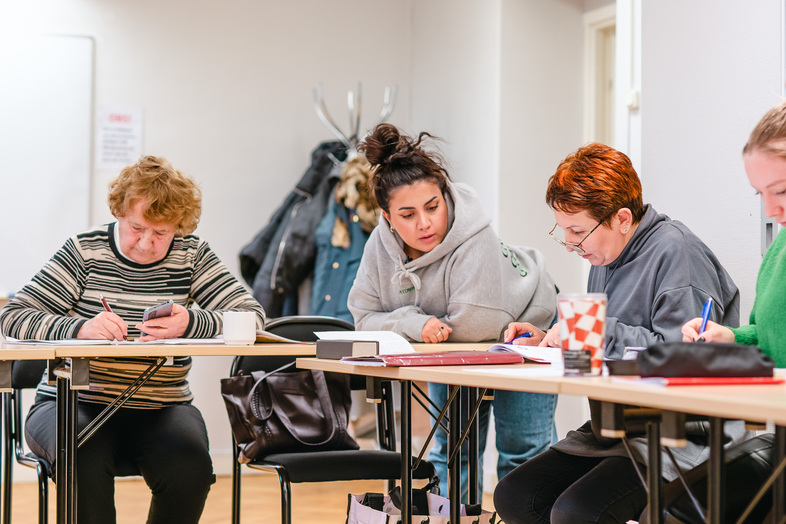 Fyra personer sitter vid ett bord och arbetar tillsammans med papper och pennor i ett klassrum.