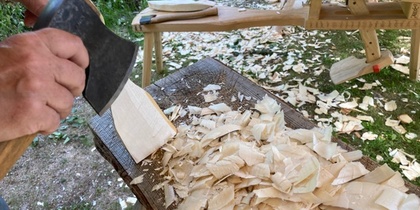 En person täljer trä med en yxa utomhus, träspån ligger på ett bord.