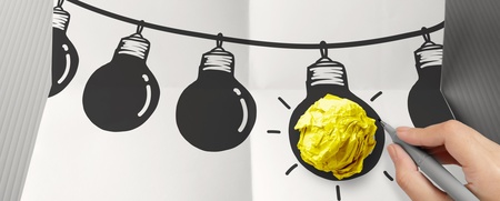 En hand ritar en glödlampa på ett papper, där en gul pappersboll används som glödlampans ljus.