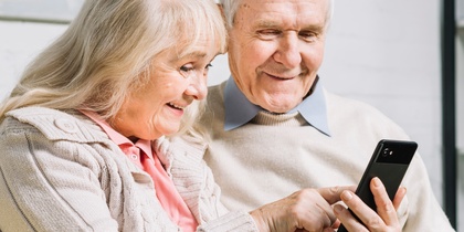 Ett äldre par sitter tillsammans i en soffa och tittar leende på en smartphone.