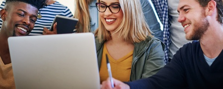 Sex unga vuxna sitter tillsammans och tittar på en bärbar dator, leende och samarbetande.