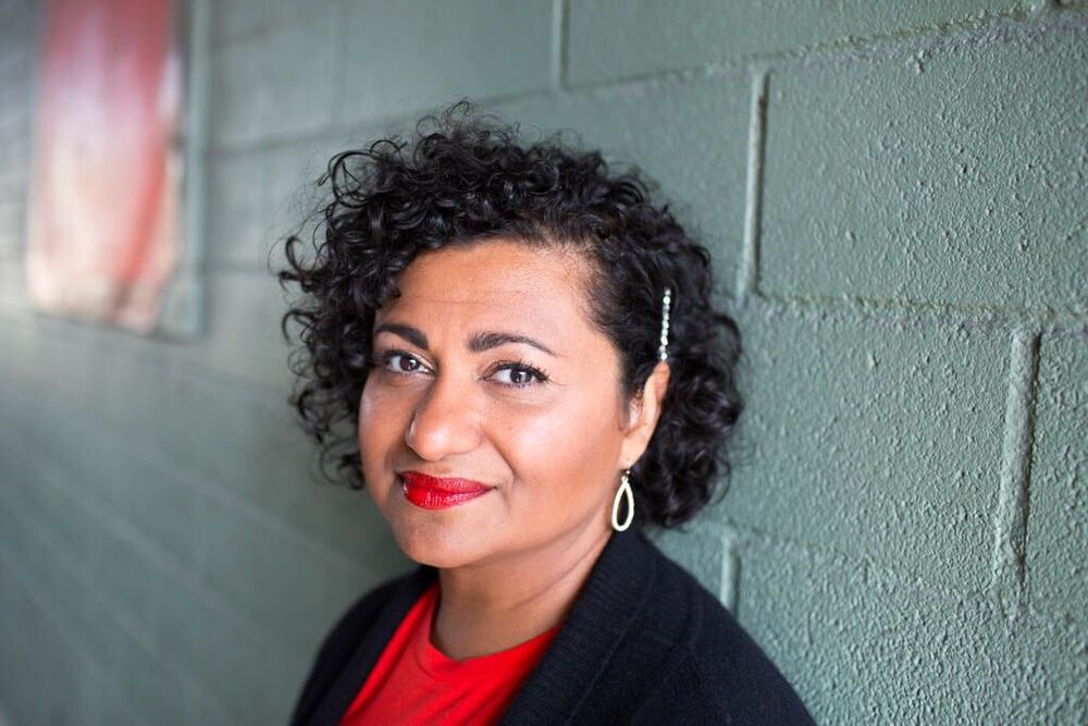 Person med lockigt hår står mot en grön tegelvägg, ansiktet är suddat för anonymitet.