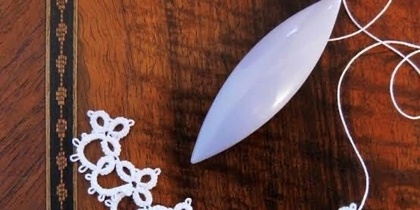 En skyttel och spetsarbete frivoliteter i vitt garn på ett träbord.